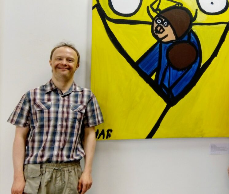 Harri Blomberg seisoo hymyillen maalauksensa vasemmalla puolella. Maalauksen nimi on Mikä on tämän kaiken järjestyksen takana.